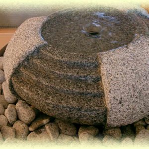 Kaskadenförmig bearbeiteter  Granit-Quellstein auf hellgrauem Zierkies in rundem Edelstahl-Becken       (Durchm.       65, Höhe 25 cm) im Detail